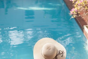back view of young woman in swimsuit and hat sitting in pool of