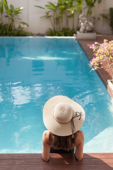 back view of young woman in swimsuit and hat sitting in pool of
