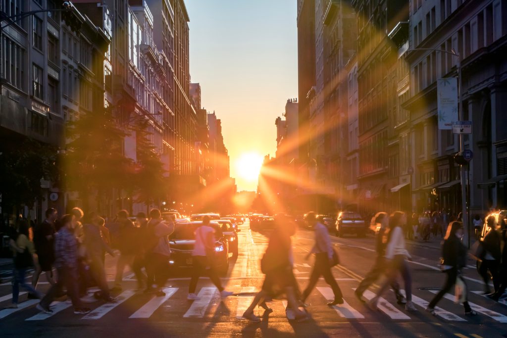 Sunlight shines over the buildings and people of a busy Midtown Manhattan street scene in New York City