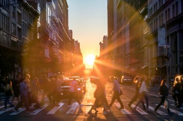 Sunlight shines over the buildings and people of a busy Midtown Manhattan street scene in New York City