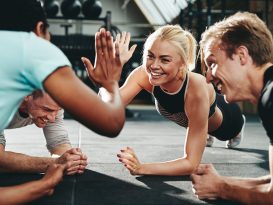 Two friends high fiving while planking on a gym floor; stronger together The Surprising Advantages of Group Fitness