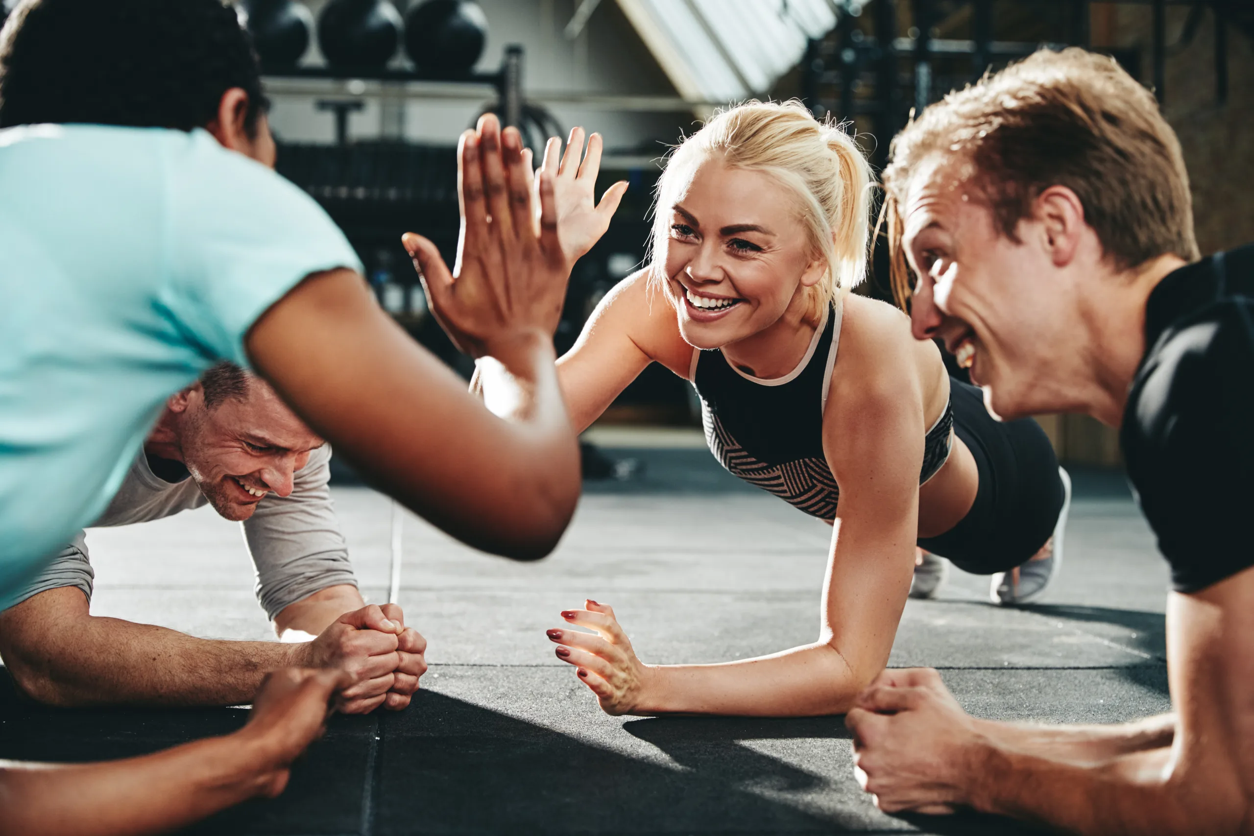 Two friends high fiving while planking on a gym floor; stronger together The Surprising Advantages of Group Fitness