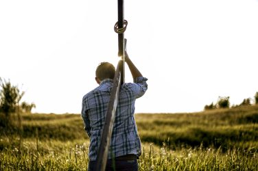 Male carrying a hand made wooden cross in a grassy field shot from behind