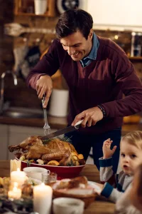 Happy father carving turkey during Thanksgiving dinner in dining room Happy father carving turkey during Thanksgiving dinner in dining room