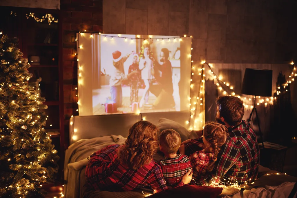 family mother father and children watching projector, film, movies with popcorn in christmas evening at home