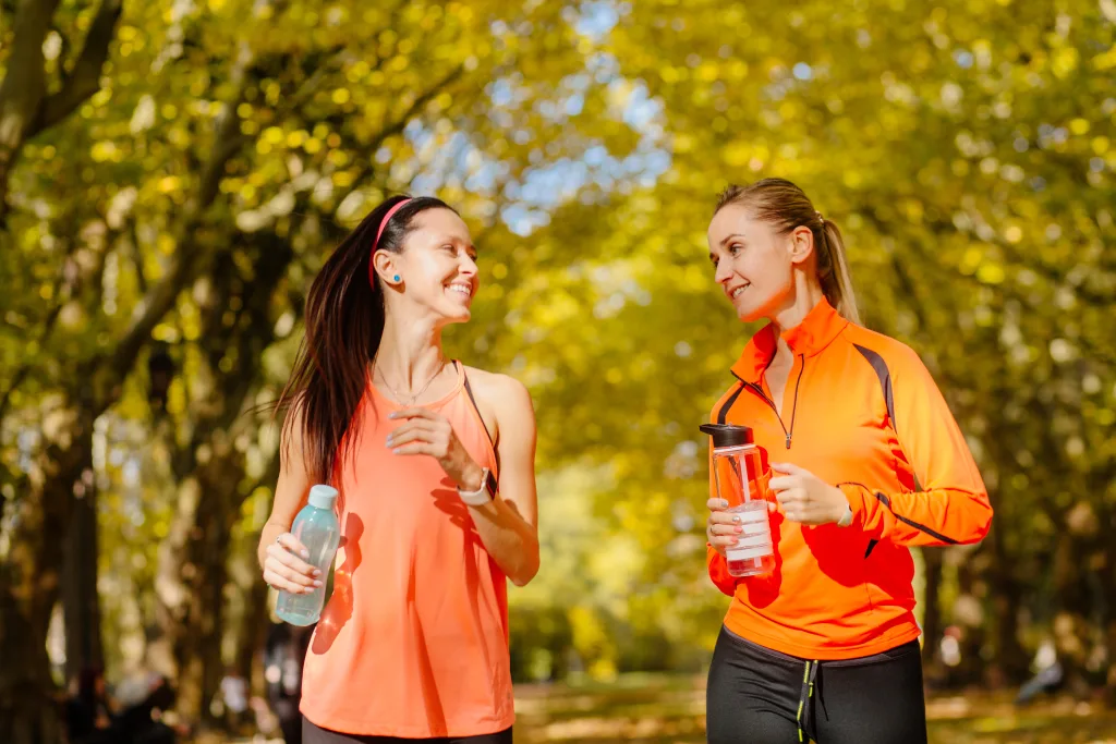 Two attractive women in their 30s are talking for a walk or jogging together outdoors Cute blonde and brunette fit women who are active and work hard to stay healthy