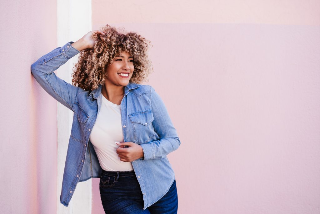 portrait of confident curvy hispanic woman leaning on pastel wall