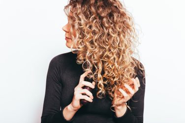 Smiling young woman applying moisturizing cosmetic oil