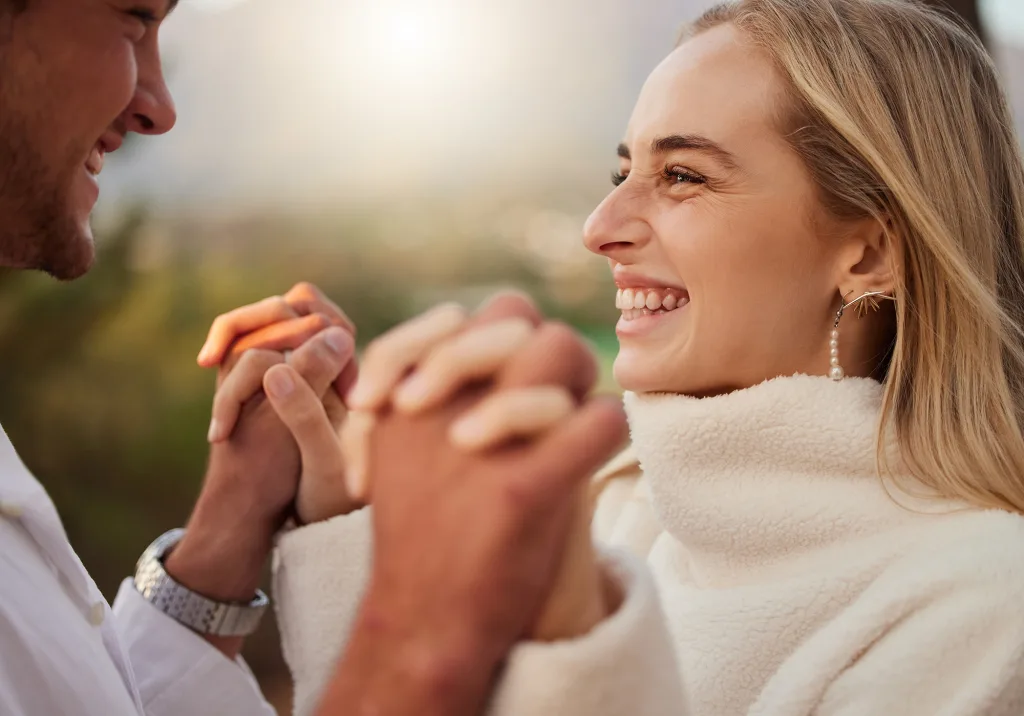 Love, couple and holding hands outdoor with a smile, care and romance on date in nature Young man and woman happy together on valentines day with trust, peace and support in forest for anniversary; Talking Points