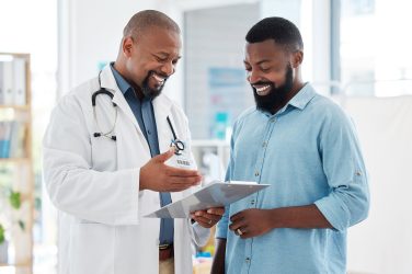 Healthcare, black man and doctor with clipboard, diagnosis and conversation for results, smile and care Male patient, guy and medical professional with documents, paperwork for insurance and talking