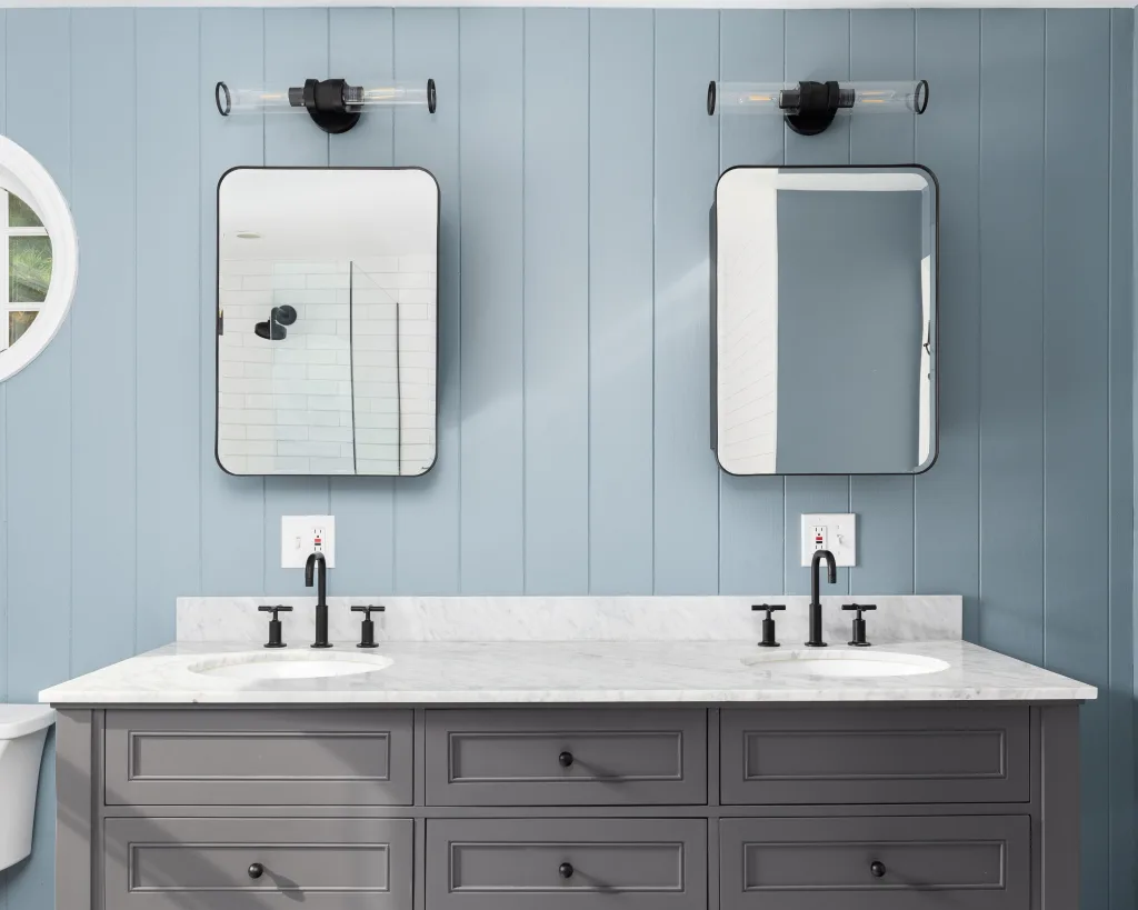 A blue wood panel bathroom with a grey cabinet, white marble countertop, and black light fixtures, mirrors, and faucets Renovation Ready Return on Your Investment with these Updates