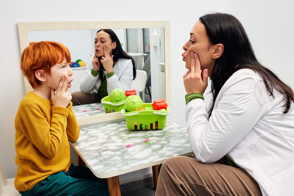 Speech therapy Therapist shaping a boy's mouth in order for his to make correct sound Speech therapy Therapist shaping a boy's mouth in order for his to make correct sound