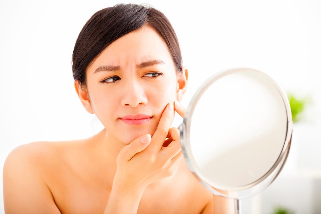 young woman Squeezing pimple looking on mirror young woman Squeezing pimple looking on mirror; Battling Breakouts | Adult Acne: Causes, Cures, and Prevention