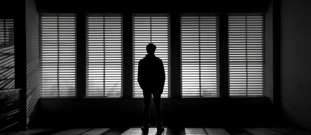 Silhouette of a Man Looking Through Blinds