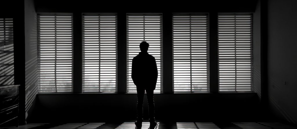 Silhouette of a Man Looking Through Blinds