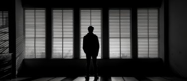Silhouette of a Man Looking Through Blinds
