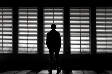 Silhouette of a Man Looking Through Blinds