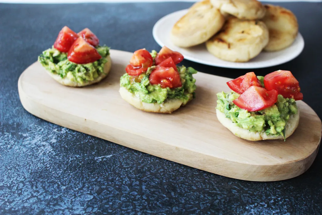 Serving board with 3 avacado arepas topped with chunks of tomatoes.