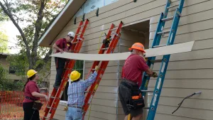 habitat for humanity construction crew and family members work together to hang siding on new home
