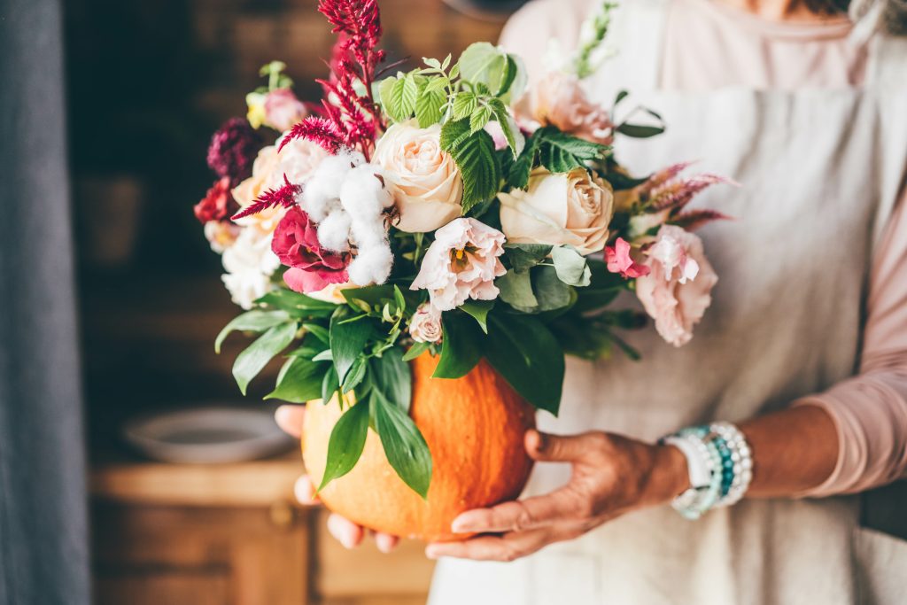 Pumpkin with beautiful bouquet of flowers in woman hands