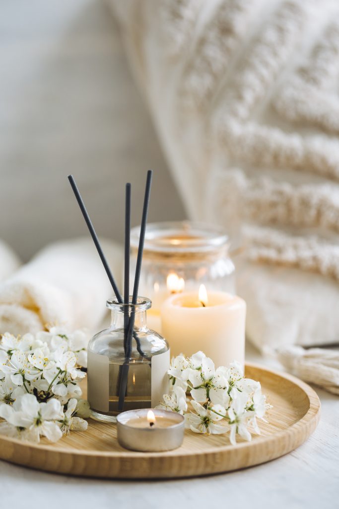 Aroma diffuser, burning candle, cherry blooming flowers and perfume on wooden bamboo tray Cozy home decor, hygge and aromatherapy concept Comfortable atmosphere, spring delicious fresh smell