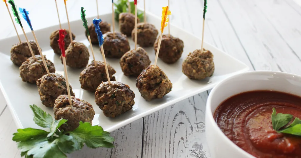 White serving dish with meatballs with toothpicks inserted and dish of marinara dipping sauce