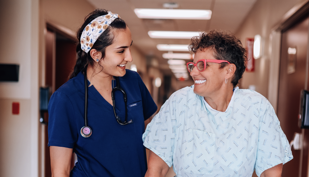 A female doctor in blue scrubs helps a breast cancer patient using a walker down the hall at Baylor Scott & White Medical Center – Grapevine