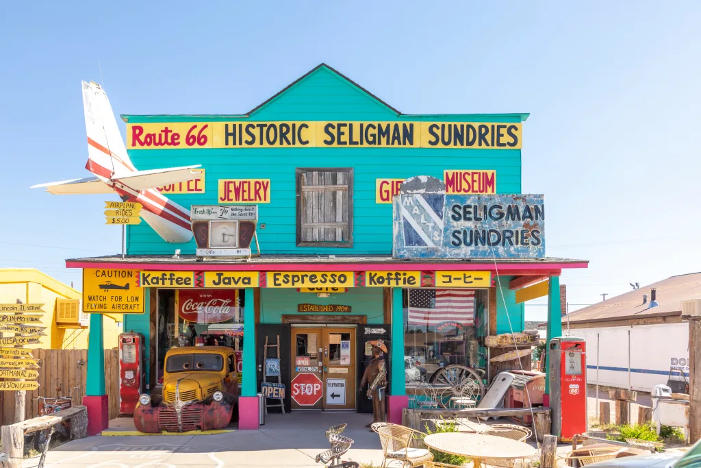 colorful facade of Shop Historic Seligman Sundries with stars and stripes and an aircraft crashed in the facade and vintage car at route 66 in Seligman, USA